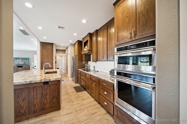 kitchen with sink, decorative backsplash, light hardwood / wood-style floors, light stone counters, and stainless steel appliances