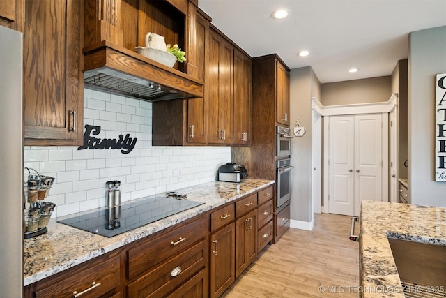 kitchen with tasteful backsplash, custom exhaust hood, black electric cooktop, light stone countertops, and light wood-type flooring