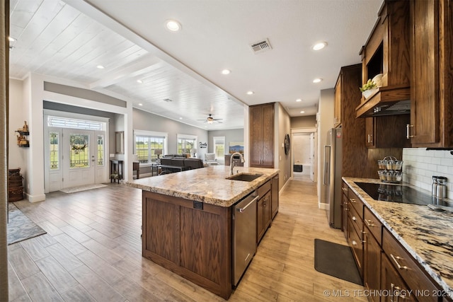 kitchen with sink, appliances with stainless steel finishes, a kitchen island with sink, backsplash, and light stone counters