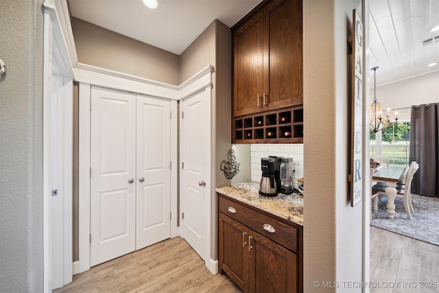 bar with tasteful backsplash, light stone counters, a notable chandelier, and light hardwood / wood-style floors