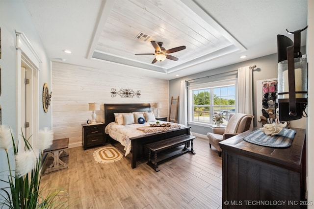 bedroom featuring wooden walls, a raised ceiling, and light hardwood / wood-style floors