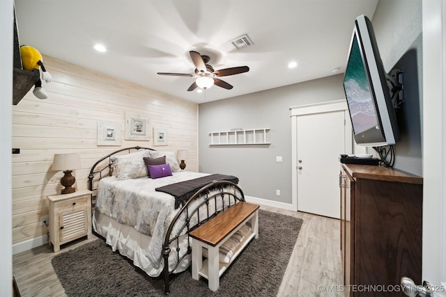 bedroom with light hardwood / wood-style flooring, ceiling fan, and wood walls