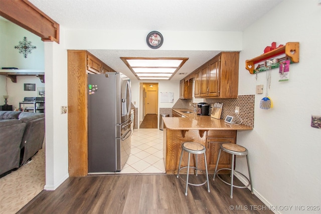 kitchen featuring sink, backsplash, stainless steel fridge, a kitchen breakfast bar, and kitchen peninsula