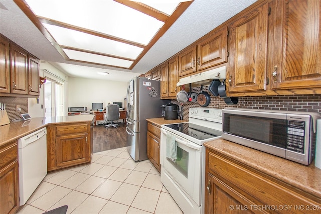 kitchen featuring light tile patterned flooring, lofted ceiling, decorative backsplash, kitchen peninsula, and white appliances