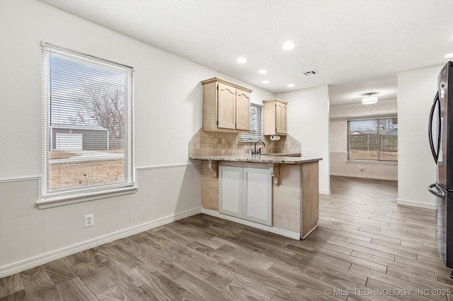 kitchen featuring tasteful backsplash, stainless steel fridge, light stone countertops, and light wood-type flooring