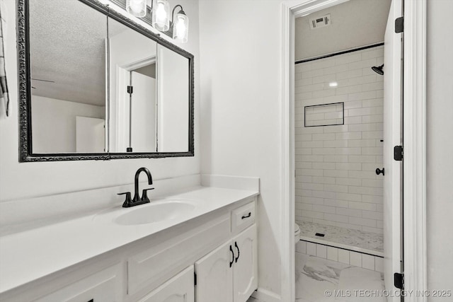 bathroom with a tile shower, vanity, toilet, and a textured ceiling