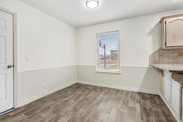 unfurnished dining area with a textured ceiling and light wood-type flooring