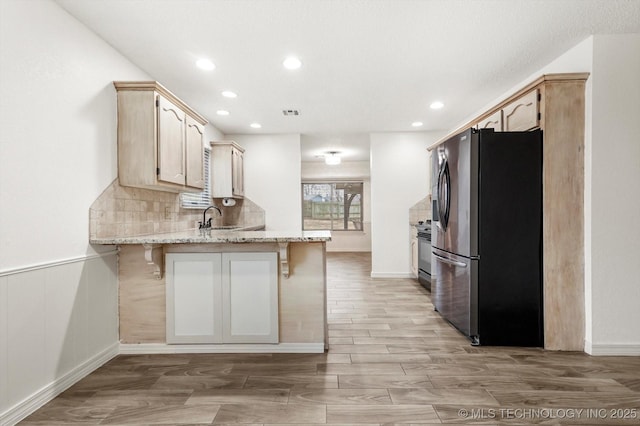 kitchen featuring stainless steel refrigerator, a kitchen bar, kitchen peninsula, and light stone counters