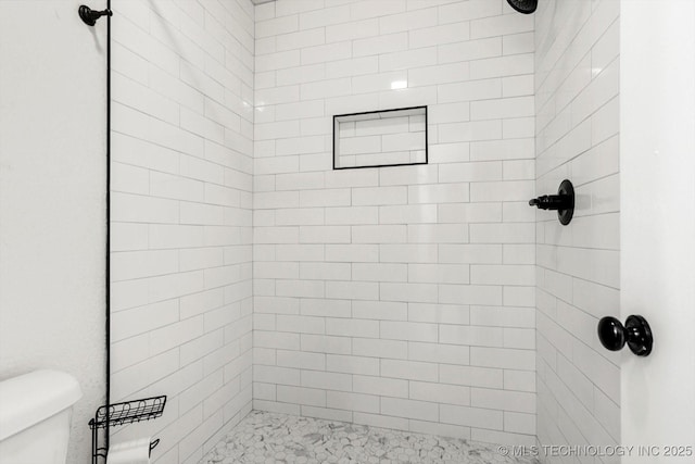 bathroom with a tile shower and toilet