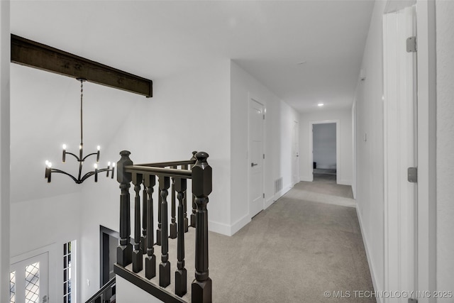 corridor featuring light colored carpet, beam ceiling, and a notable chandelier