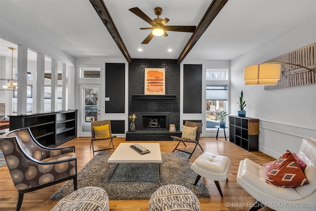 living room with ceiling fan, a large fireplace, beamed ceiling, and light wood-type flooring