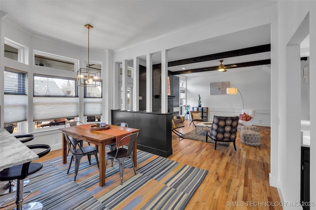 dining space with beamed ceiling, a notable chandelier, crown molding, and light wood-type flooring