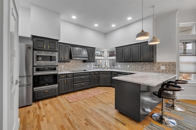 kitchen with premium range hood, a kitchen bar, hanging light fixtures, kitchen peninsula, and stainless steel appliances