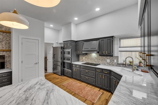 kitchen featuring appliances with stainless steel finishes, pendant lighting, sink, light stone counters, and wall chimney exhaust hood