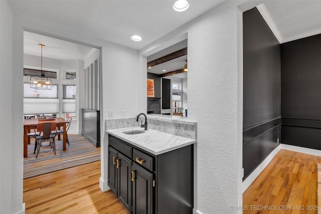 kitchen featuring hanging light fixtures, crown molding, sink, and light hardwood / wood-style flooring