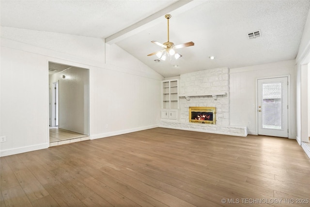 unfurnished living room featuring lofted ceiling with beams, a stone fireplace, ceiling fan, and light hardwood / wood-style flooring