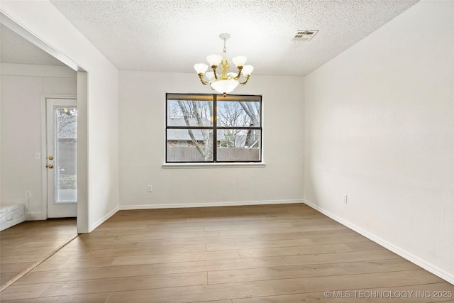 unfurnished dining area with a chandelier, hardwood / wood-style floors, a textured ceiling, and a wealth of natural light