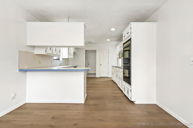 kitchen with white cabinetry, dark hardwood / wood-style flooring, kitchen peninsula, and a textured ceiling