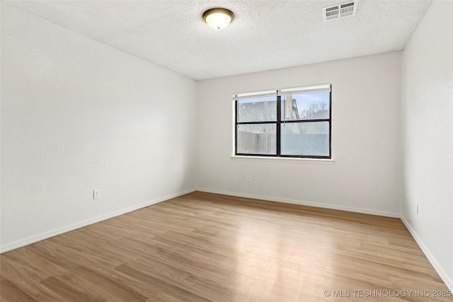 empty room with a textured ceiling and light hardwood / wood-style floors