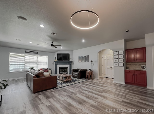 living room with ceiling fan, a brick fireplace, a textured ceiling, and light hardwood / wood-style floors