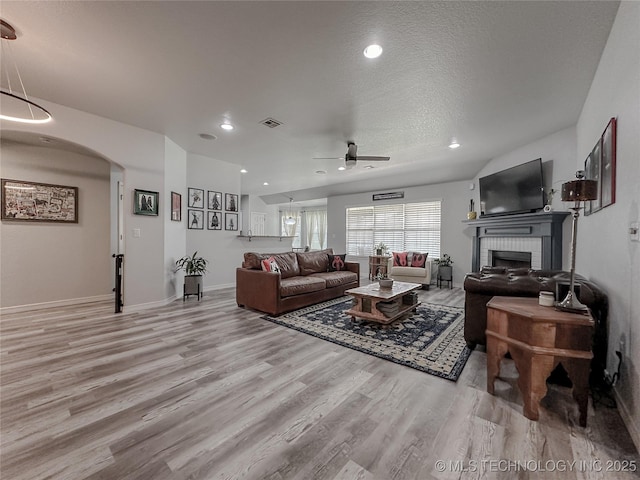 living room featuring a brick fireplace, light hardwood / wood-style flooring, a textured ceiling, and ceiling fan