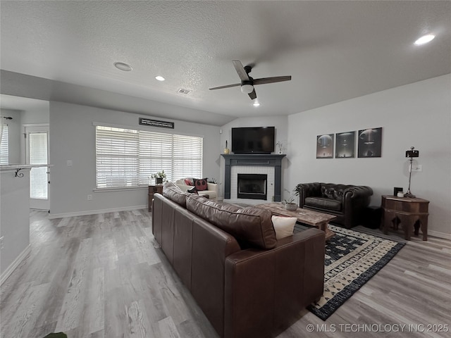 living room with ceiling fan, a fireplace, light hardwood / wood-style floors, and a textured ceiling