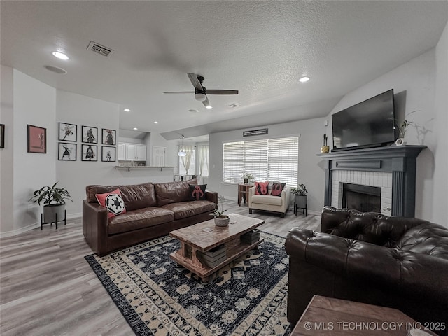 living room with ceiling fan, a fireplace, light hardwood / wood-style floors, and a textured ceiling