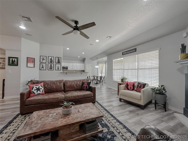 living room featuring ceiling fan, light hardwood / wood-style floors, and a textured ceiling