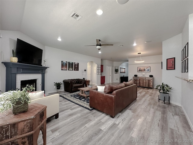 living room with ceiling fan, a fireplace, light hardwood / wood-style floors, a textured ceiling, and vaulted ceiling