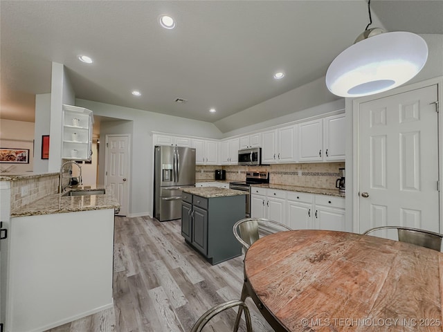 kitchen featuring a kitchen island, appliances with stainless steel finishes, white cabinetry, sink, and light stone counters