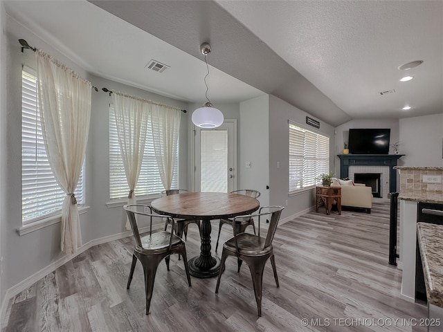 dining space featuring a brick fireplace, a textured ceiling, and light hardwood / wood-style flooring