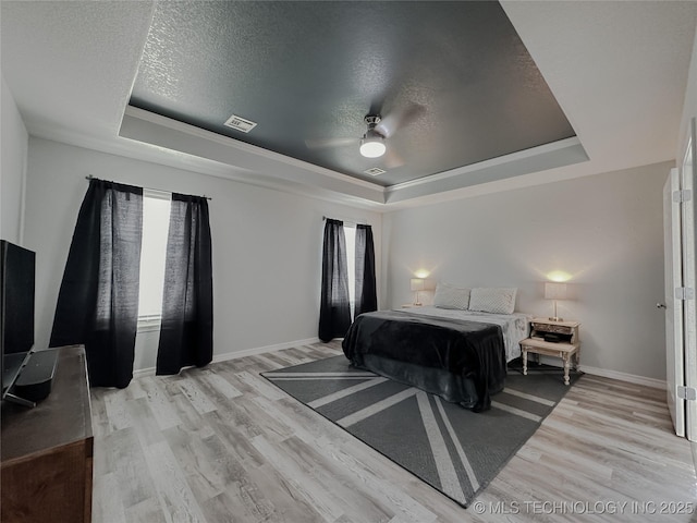 bedroom featuring a textured ceiling, light hardwood / wood-style floors, and a tray ceiling