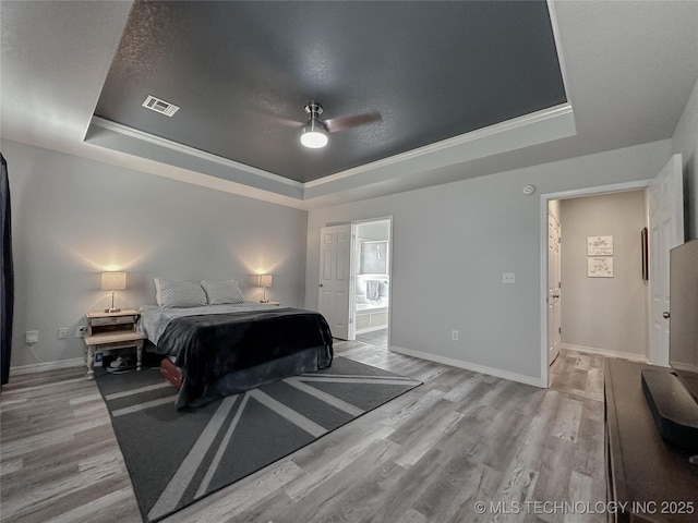 bedroom with connected bathroom, a tray ceiling, and light hardwood / wood-style flooring