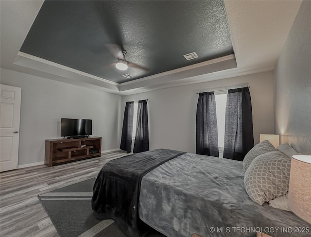 bedroom with crown molding, ceiling fan, hardwood / wood-style floors, a textured ceiling, and a raised ceiling