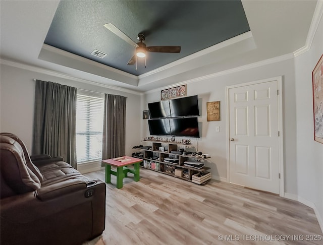 living room with ornamental molding, a raised ceiling, ceiling fan, and light wood-type flooring