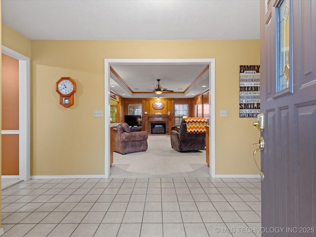 tiled entryway with ceiling fan, a fireplace, and a raised ceiling