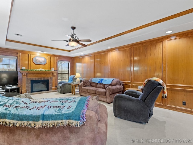 carpeted living room featuring crown molding, a tray ceiling, a fireplace, and ceiling fan