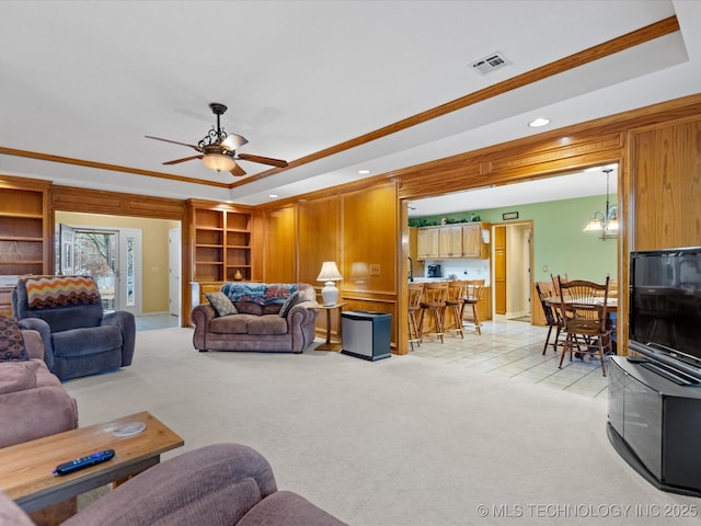 carpeted living room with crown molding, a tray ceiling, and ceiling fan with notable chandelier