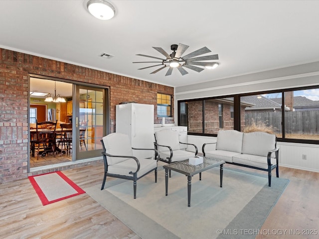 interior space with ceiling fan with notable chandelier, light wood-type flooring, and brick wall