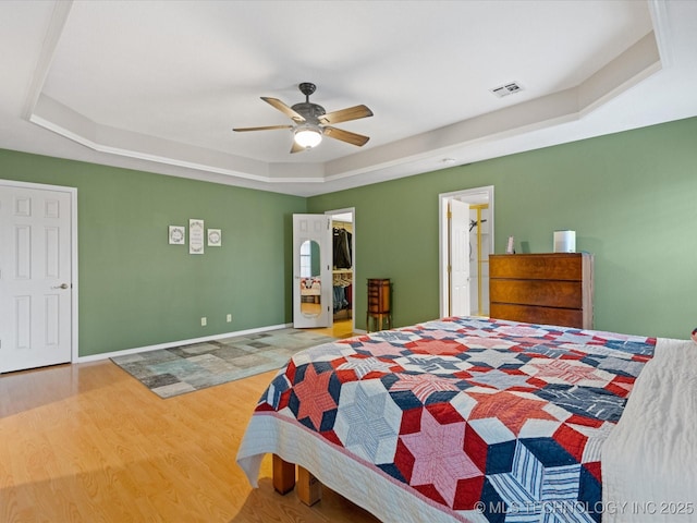 bedroom featuring wood-type flooring, a spacious closet, a tray ceiling, a closet, and ceiling fan