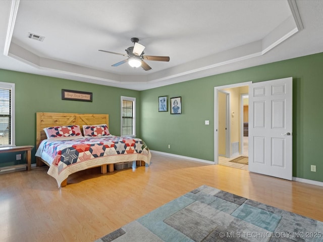 bedroom featuring multiple windows, hardwood / wood-style floors, and a tray ceiling