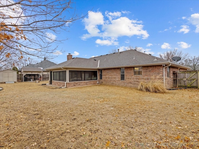 rear view of property with a sunroom, a yard, and a storage unit