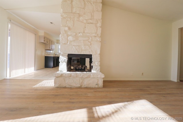 unfurnished living room with vaulted ceiling, a stone fireplace, and light hardwood / wood-style floors