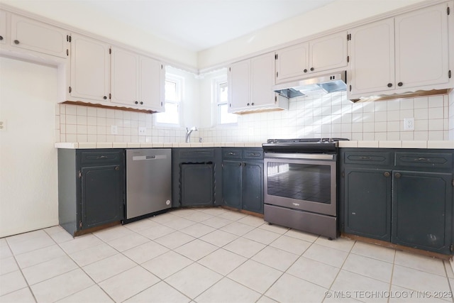 kitchen with appliances with stainless steel finishes, white cabinets, decorative backsplash, tile counters, and light tile patterned floors