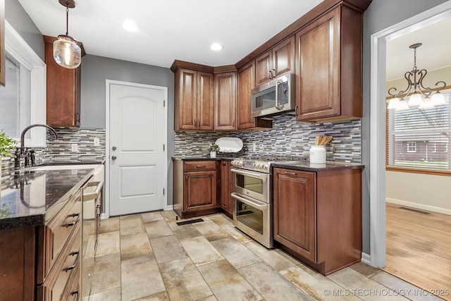 kitchen with sink, dark stone counters, pendant lighting, stainless steel appliances, and backsplash