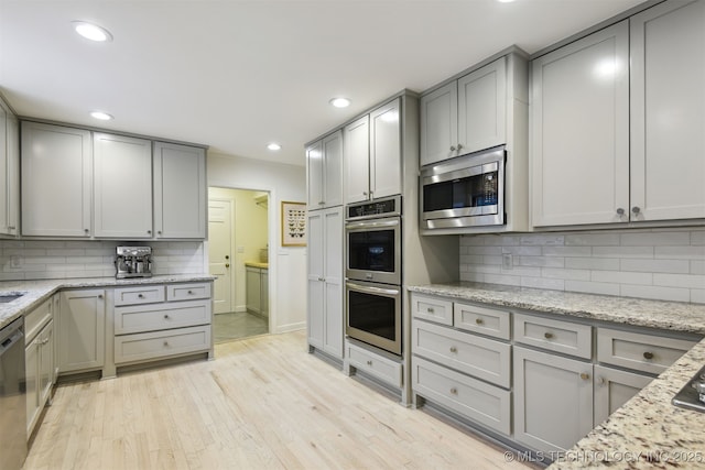 kitchen featuring light stone counters, stainless steel appliances, gray cabinets, and light wood-type flooring