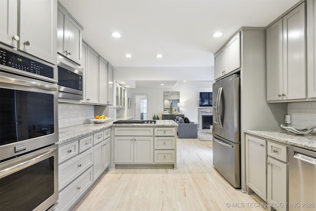 kitchen featuring appliances with stainless steel finishes, light stone countertops, light hardwood / wood-style flooring, and gray cabinetry