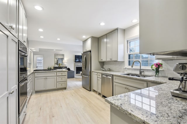 kitchen with tasteful backsplash, sink, light stone counters, stainless steel appliances, and light hardwood / wood-style flooring