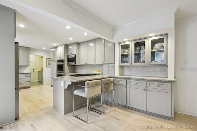 kitchen with stainless steel appliances, light stone countertops, gray cabinetry, and kitchen peninsula