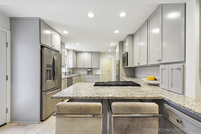 kitchen with stainless steel appliances, kitchen peninsula, light stone countertops, and gray cabinetry